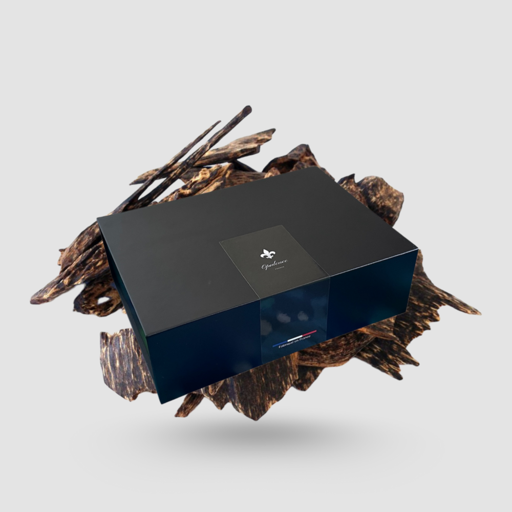 Coffret cadeau Opulence noir mat en lévitation avec copeaux de bois de Oud en arrière plan.