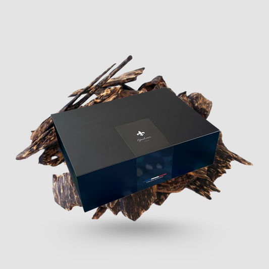 Coffret cadeau Opulence noir mat en lévitation avec copeaux de bois de Oud en arrière plan.
