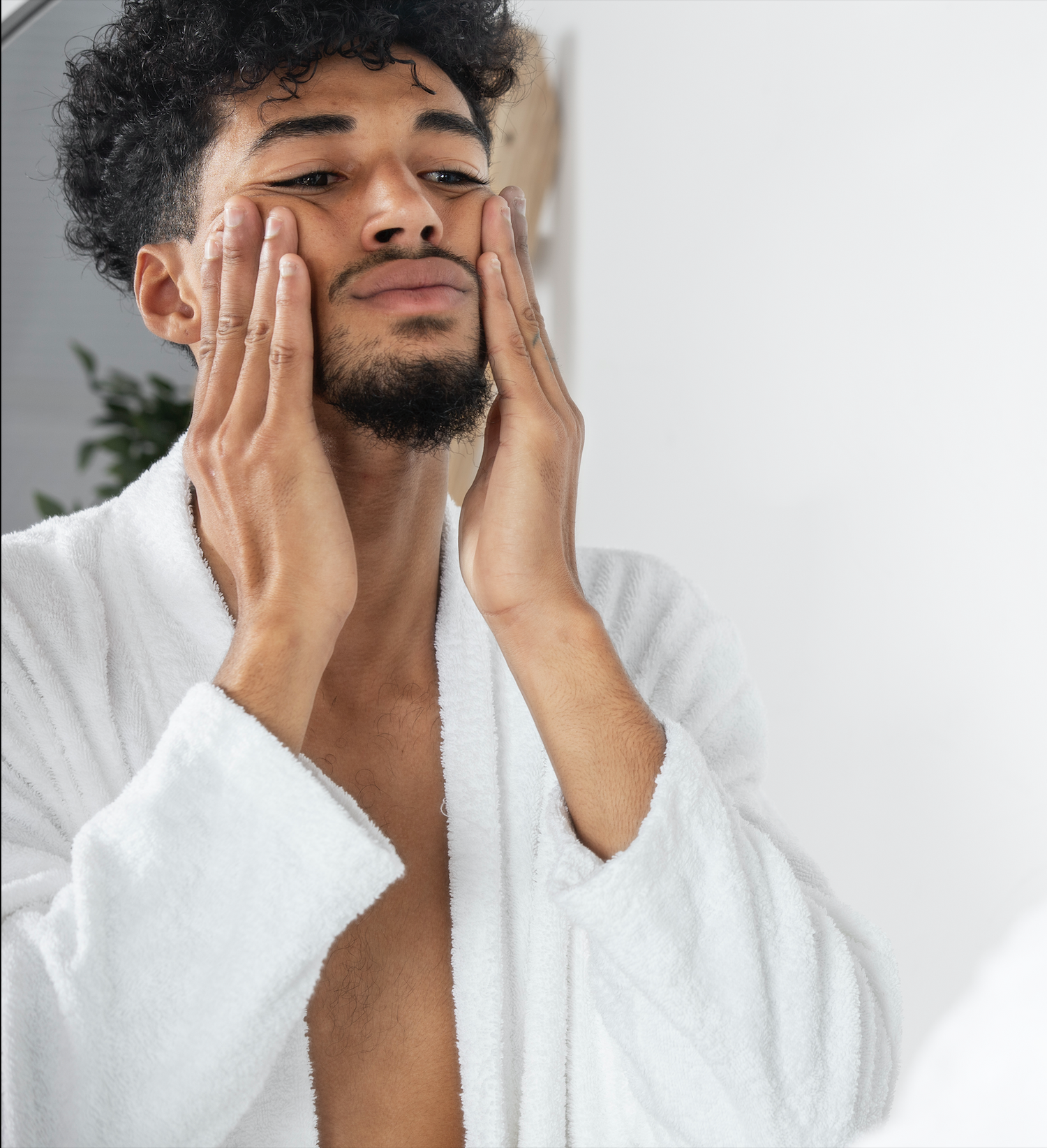 Jeune homme élégant en peignoir qui applique un soin sur son visage.